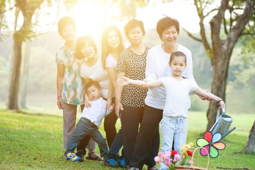Large group of happy Asian multi generations family playing at park, grandparent, parent and children, outdoor nature park in morning with sun flare.