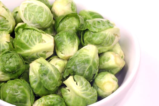 Fresh raw green Brussels sprouts are in white plate on white background.