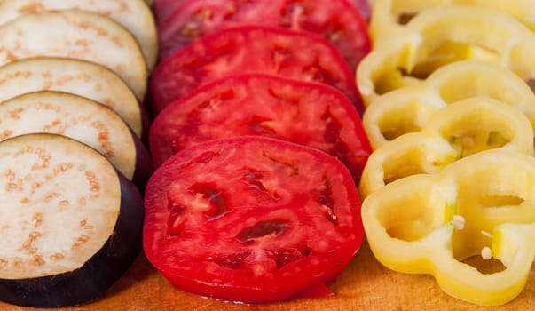 Sliced eggplant tomato and sweet pepper on wooden cutting board