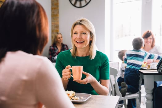 Women are sitting at a table in a cafe, socialising over coffee and tea.