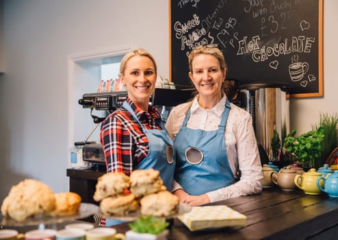 Friendly waitresses is standing behind the counter in the cafe she works in and is smiling for the camera.