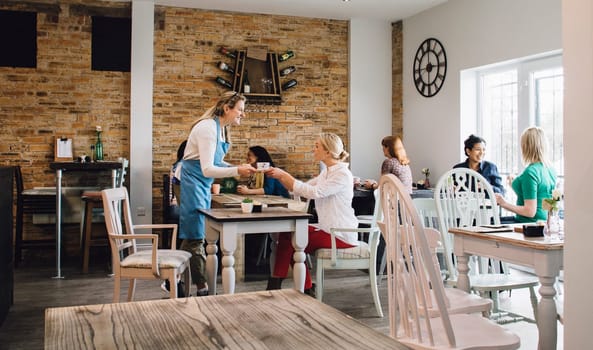 Waitress is serving a cup of tea to a customer sitting at a table in a cafe.