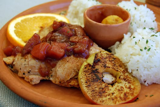 Turkey meat with different fruits and rice on earthenware plate.