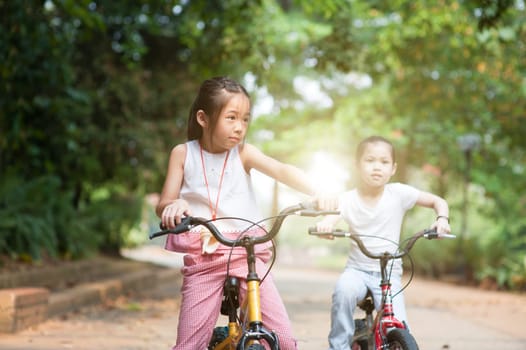 Portrait of active Asian family at nature park. Children cycling outdoors. Morning sun flare background.