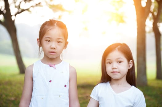 Portrait of Asian children at park. Little girls having fun outdoors. Morning sun flare background.