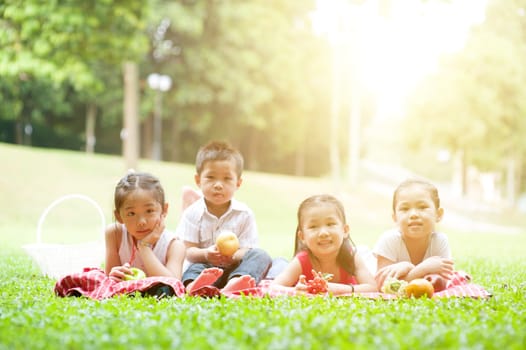 Portrait of Asian children picnics at park, lying on lawn. Kids having fun outdoors. Morning sun flare background.