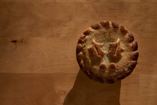 Single mince pie shot directly from above on wooden table, with lots of copy space
