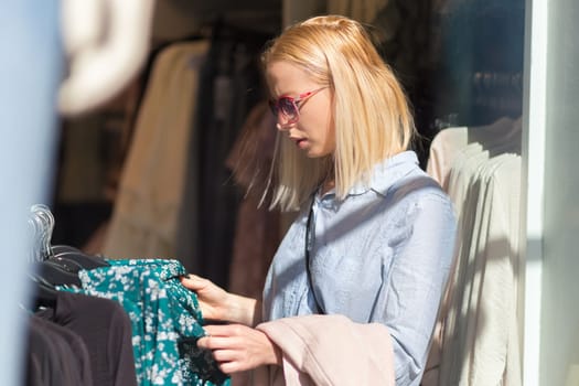 Woman shopping clothes. Female shopper looking at fashionable clothes indoors in clothing store.