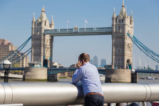 Businessman talking on mobile phone outdoor, looking at Tower Bridge in London city, UK.