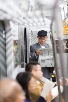 Tokyo, Japan - November 6, 2015: Japanese businessman taking ride to work, standing inside public transport and reading newspaper on November 6th in Tokyo, Japan, 2015 .