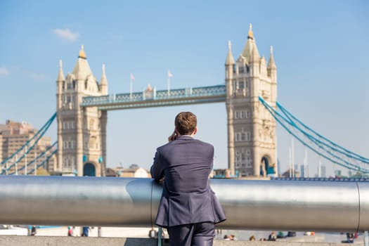 Businessman talking on mobile phone outdoor, looking at Tower Bridge in London city, UK.