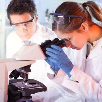Life scientists researching in laboratory. Female young scientist and her post doctoral supervisor microscoping in their working environment. Healthcare and biotechnology.