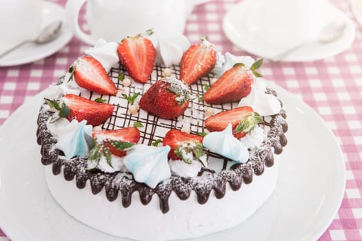 Tasty strawberry cream cake on checkered table, with tea set