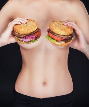Young naked woman keep in her hands two tasty burgers.