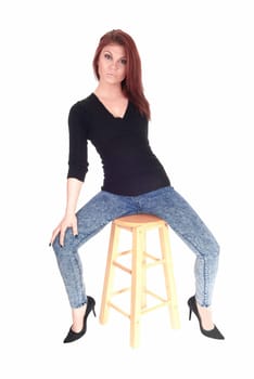 A beautiful young woman in jeans and a black sweater sitting on an bar.chair with her legs spread, isolated for white background..