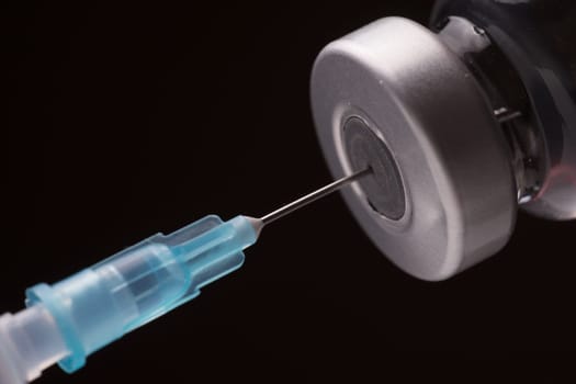 Medical syringe with the needle in the vial. Isolated on black background