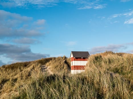 Small red and white striped hut standing on the beach dunes with sea views