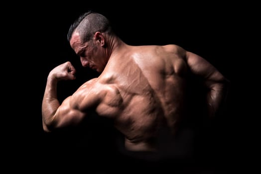 Power athletic man with great physique. Strong bodybuilder showing his biceps.