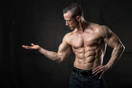 Power athletic man with great physique with raised hand redy to hold some product.