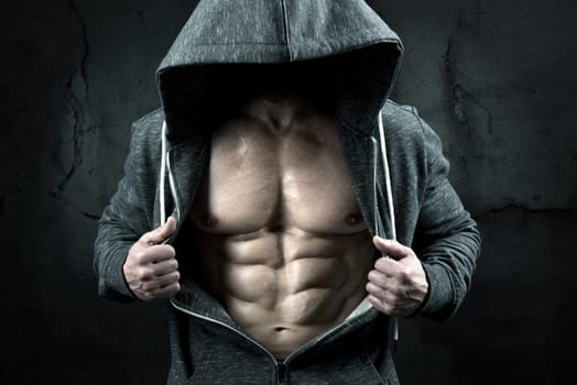 Power athletic man with hoodieshowing six pack, perfect abs over a grunge background