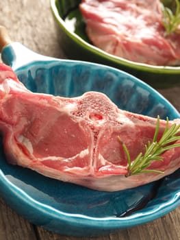 Raw lamb chop with rosemary in rustic bowls on wood
