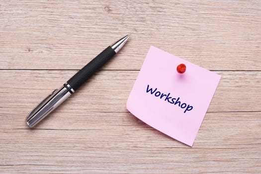 Word workshop on pink sticky note with red pin and ballpoint pen