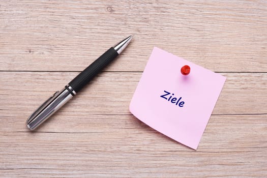 Text targets on pink sticky note with ballpoint pen on wood