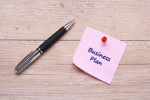Handwriting Business Plan on pink sticky note with ballpoint pen