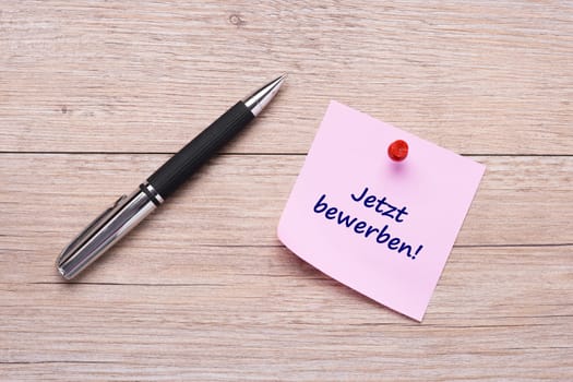 Apply text now on pink sticky note and ballpoint pen on wood