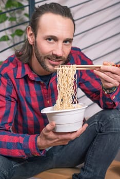 young man in checkered shirt sitting on stairs and eating asian food