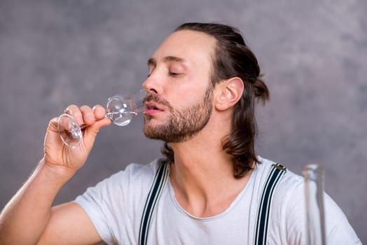 young man in front of gray background drinking clear spirit