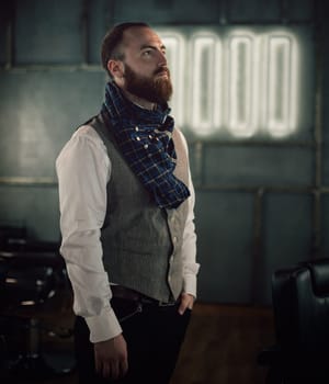 Handsome bearded man hipster with stylish beard in white shirt and chekered scarf standing with serious face in beauty salon or barbershop