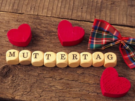 Mothers Day background with the German word Mothersday on wooden dices, red heart shapes and bow decoration