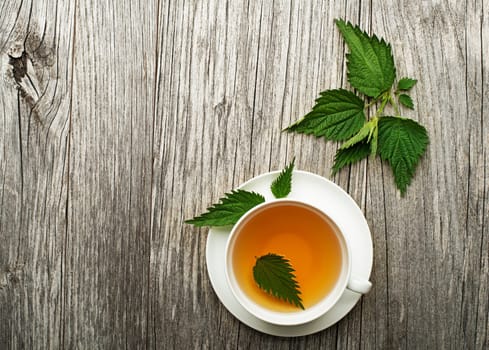Cup of healthy herbal tea with nettle on wooden background.