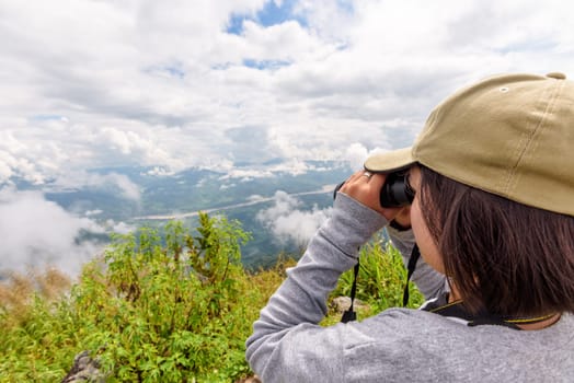 Woman tourist are using binoculars to see the beautiful natural landscape of the sky forest and mountain near the Mekong River at Doi Pha Tang view point in Chiang Rai Province, Thailand