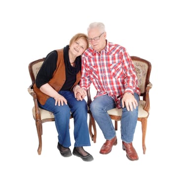 An older senior citizen couple sitting in two chairs, the wife with her .head on the shoulder of her husband, isolated for white background..