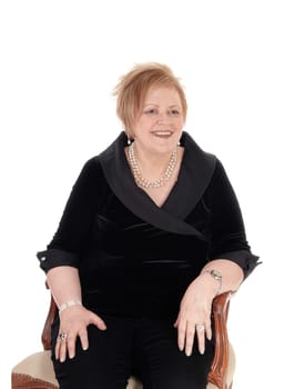 A happy smiling senior citizen woman in a black suit sitting in an old.armchair, relaxing, isolated for white background..