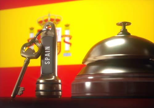 Luxury hotel key and vintage golden bell of the Spain on the wooden table of the lobby service.