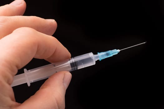 Hand holding a syringe, the syringe is filled with clear liquid and the photo is isolated on black background