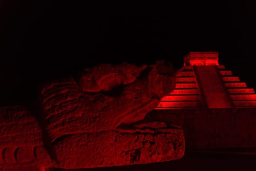 Snake head and pyramid of Chichen Itza at night bathed in beautiful red light in Mexico