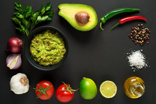 Avocado guacamole with fresh ingredients on black table