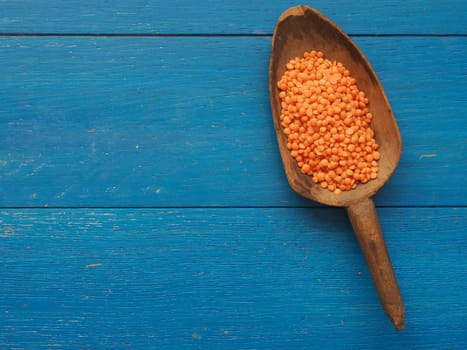 Rustic wooden spoon with red lentils on a blue wooden table