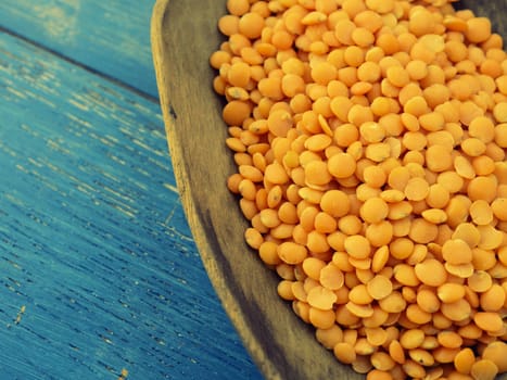 Rustic wooden spoon with red lentils on a blue wooden table, vintage color toned close up shot