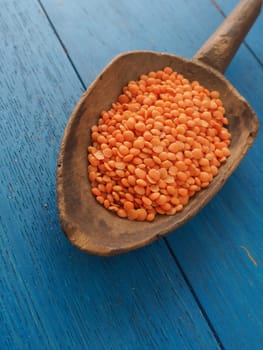 Rustic wooden spoon with red lentils on a blue wooden table