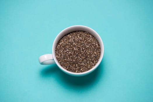 Nutritious chia seeds in cup on light blue background.