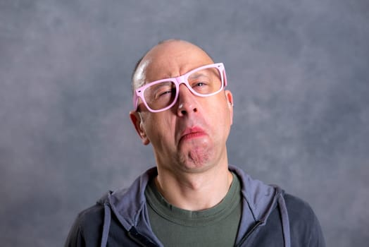 funny baldheaded man with pink glasses in front of gray background