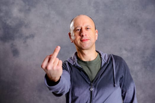 young baldheaded man in front of gray background showing middle finger