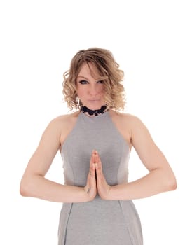 A lovely blond woman standing in a gray dress with her hands .folded, praying, isolated for white background..
