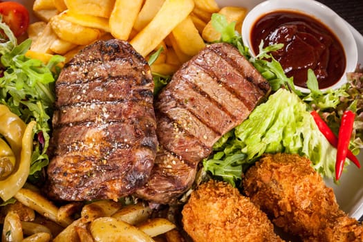 Huge barbecue plate with mixed meat and steaks on salad