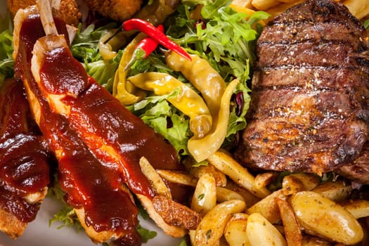 Huge barbecue plate with mixed meat and steaks on salad